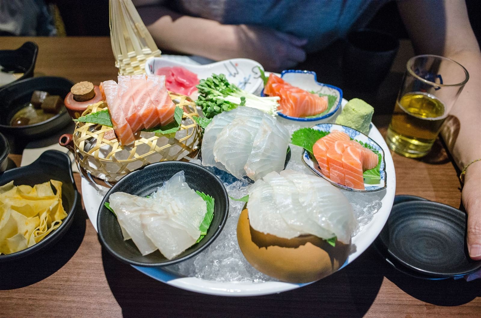 A restaurant table set with a platter of fresh raw fish (hoe), side dishes, and a glass of beer