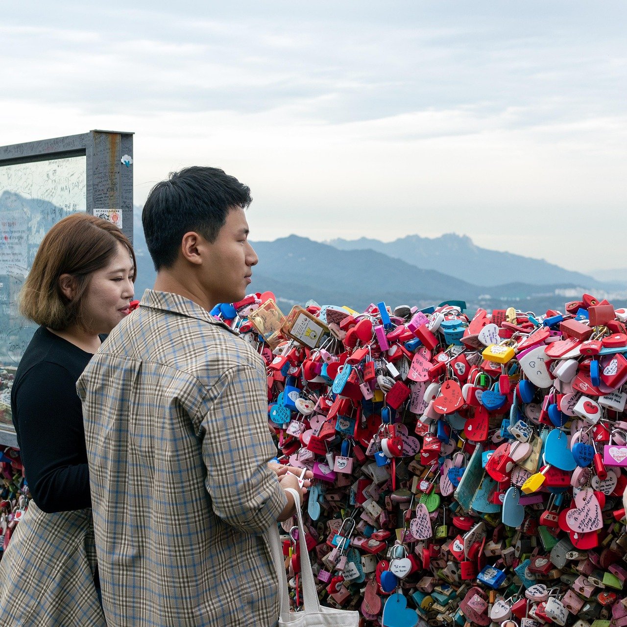 A couple looking at a wall covered in colorful love locks with mountains in the background