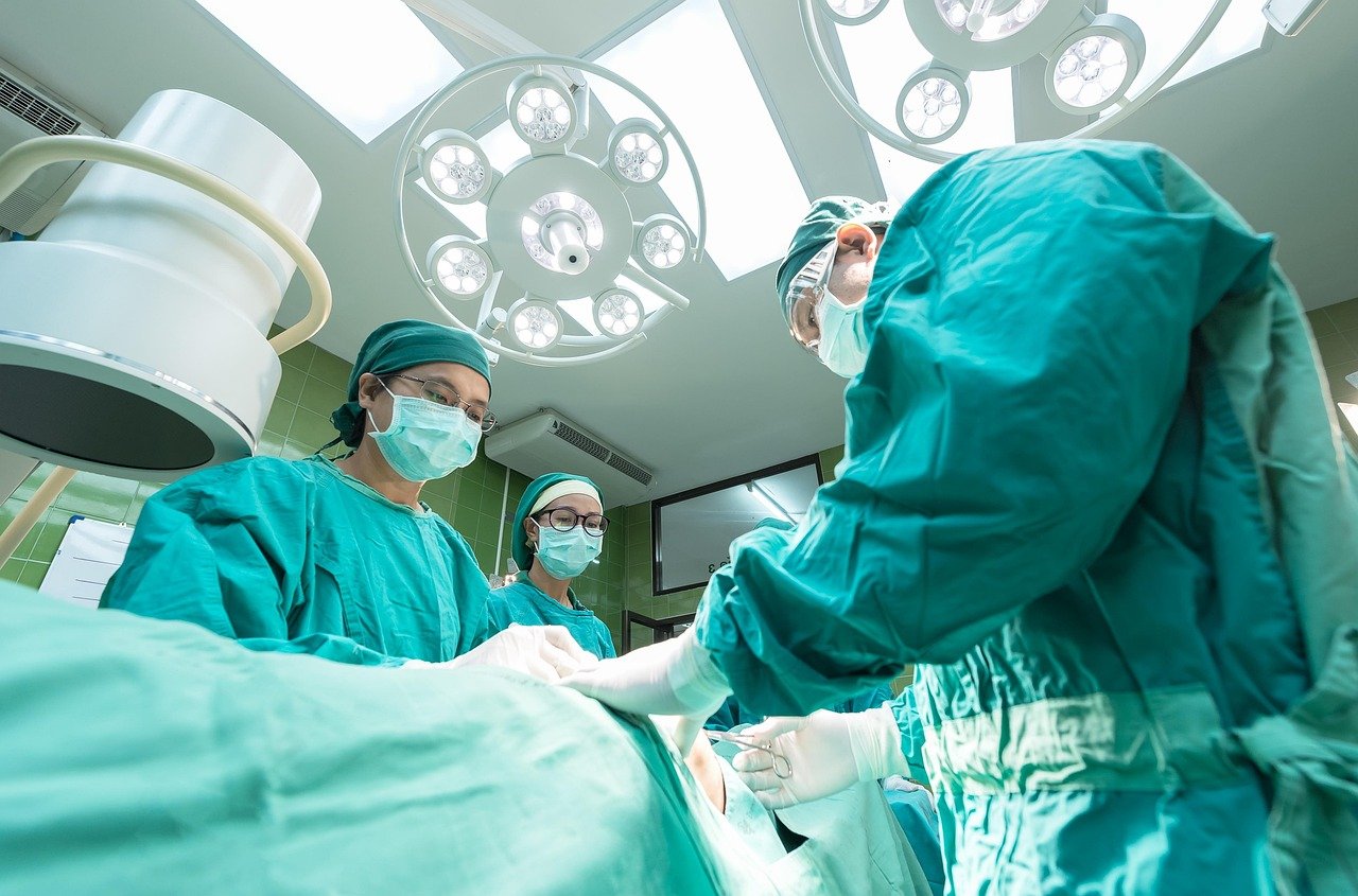 Medical team in green surgical scrubs working under operating room lights in a hospital