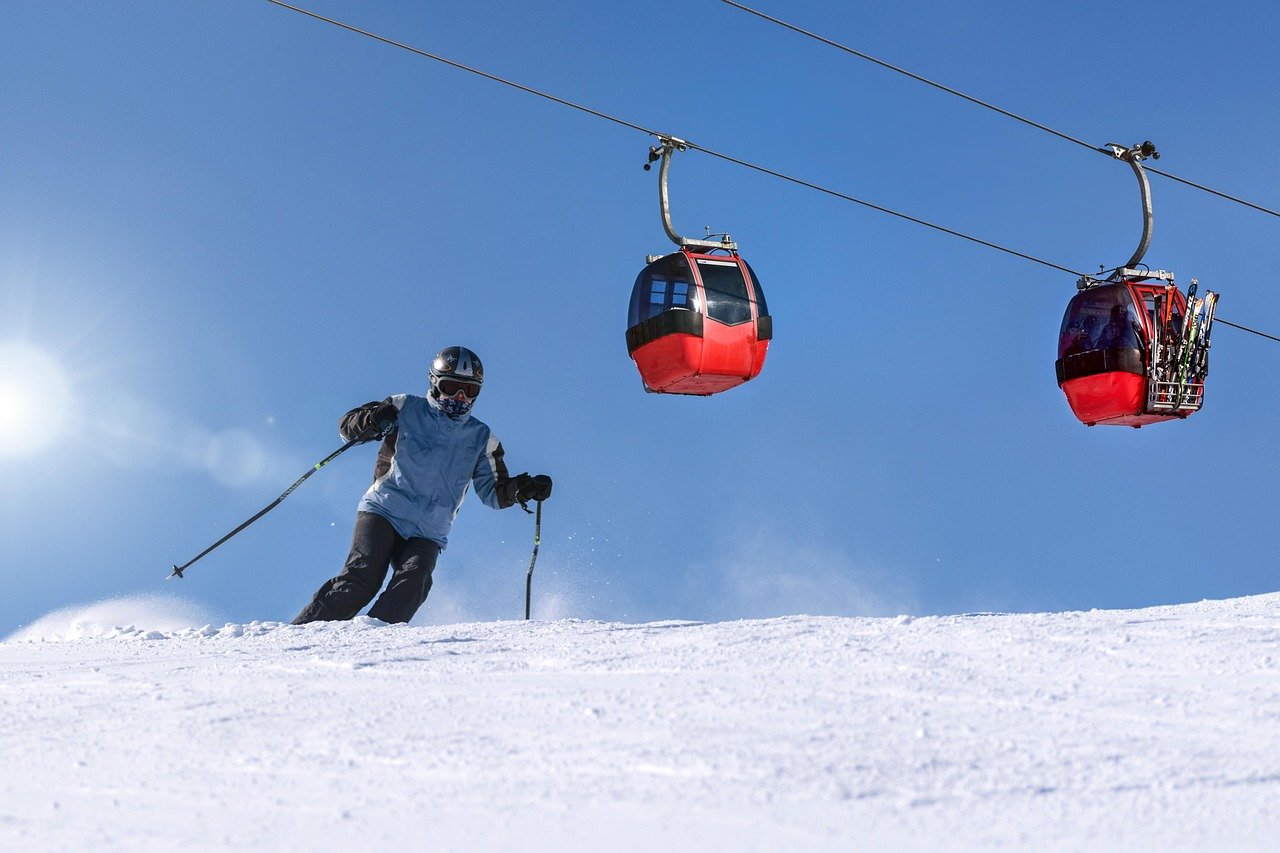 Skier on a sunny snow-covered slope with a gondola lift overhead