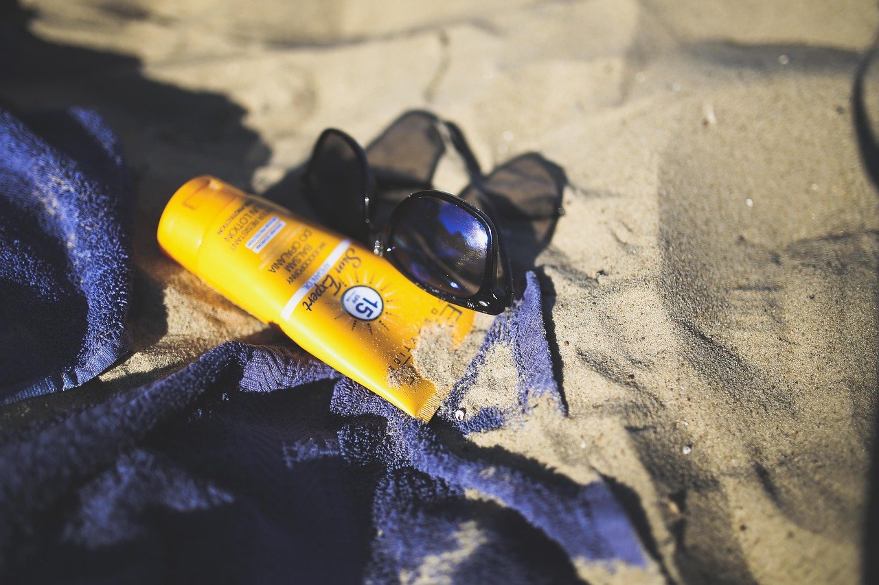 Sunscreen tube with SPF label lying next to sunglasses on sand