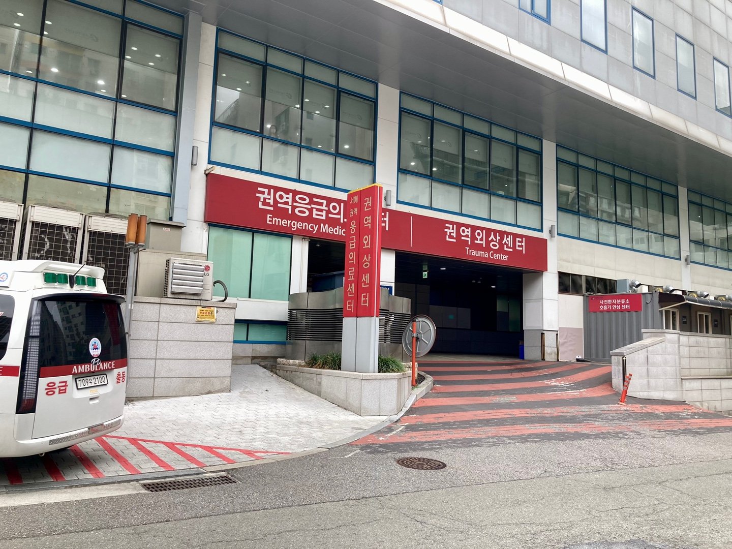 Close-up of a Korean hospital's Regional Emergency Medical Center and Trauma Center sign in Korean and English, with an ambulance parked below