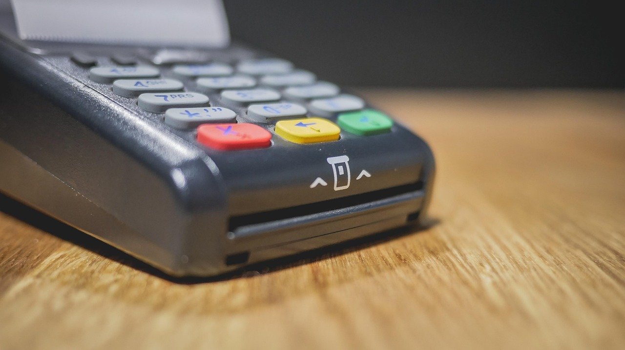 A card payment terminal on a wooden counter with a receipt feeding out of it