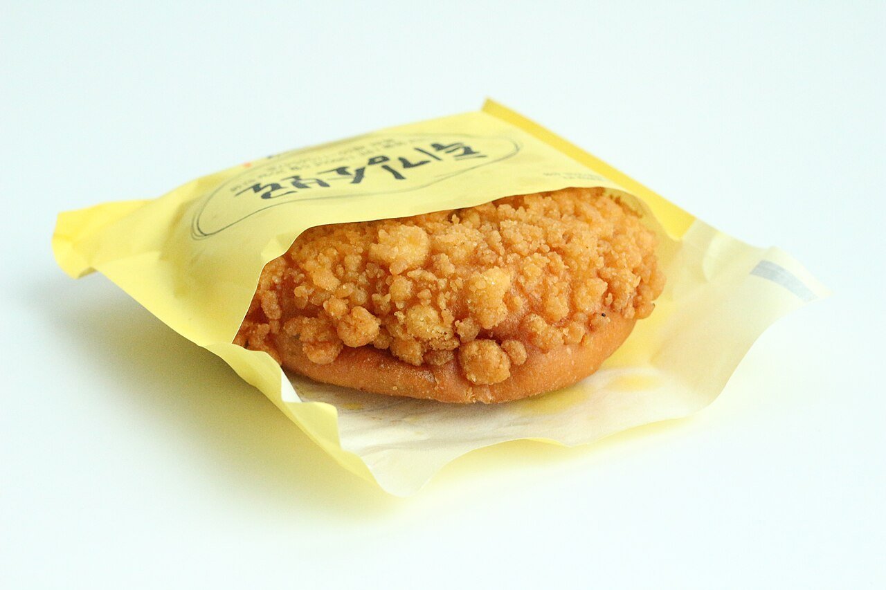 A twigim-soboro bun in its yellow Sungsimdang wrapper, the fried crumb topping deep gold and craggy