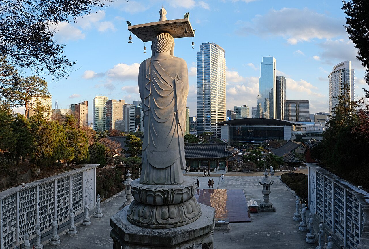 The giant stone Buddha at Bongeunsa seen from behind, with the Gangnam skyline and the COEX convention centre directly beyond it