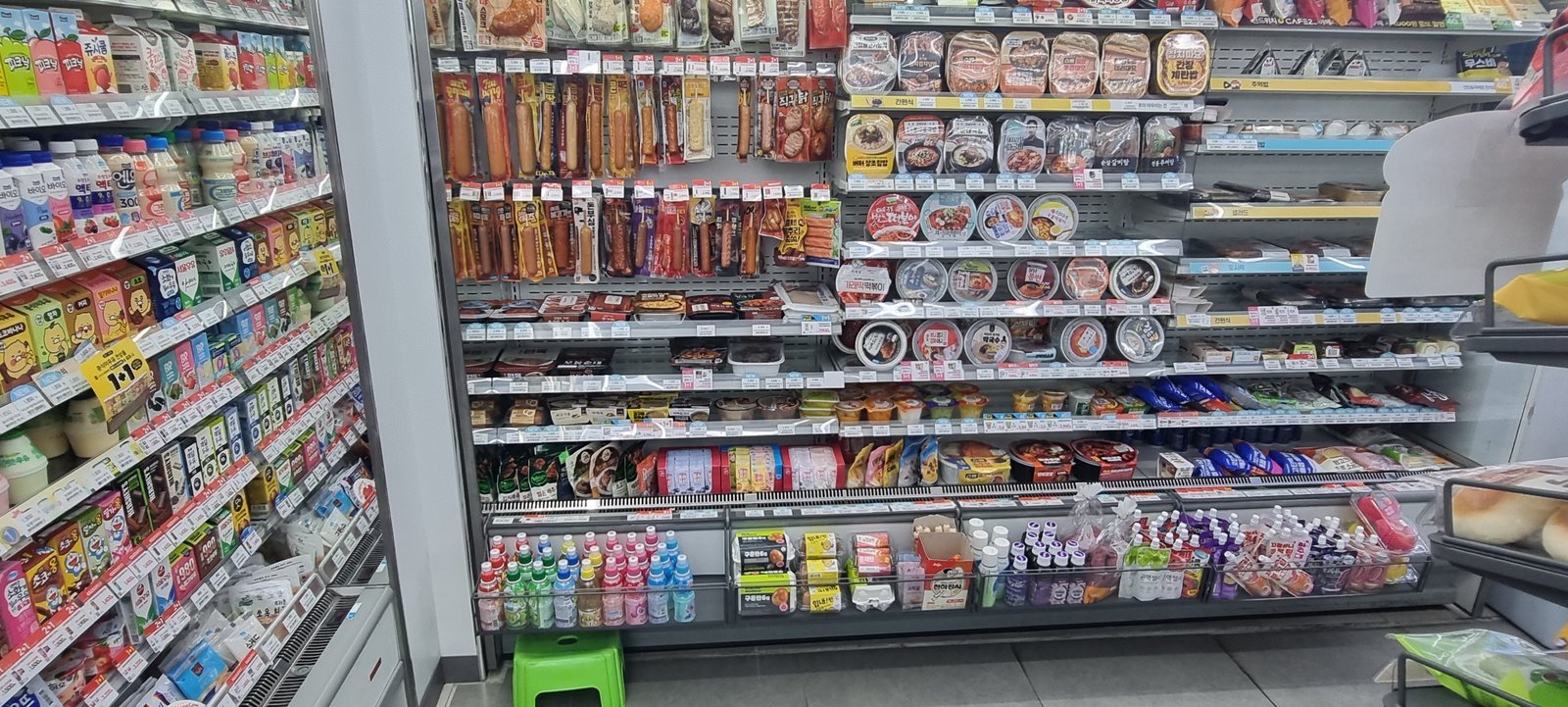 Ready-to-eat food shelves inside a Korean convenience store, stocked with gimbap, lunch boxes, sausages, cup ramen and yogurt drinks