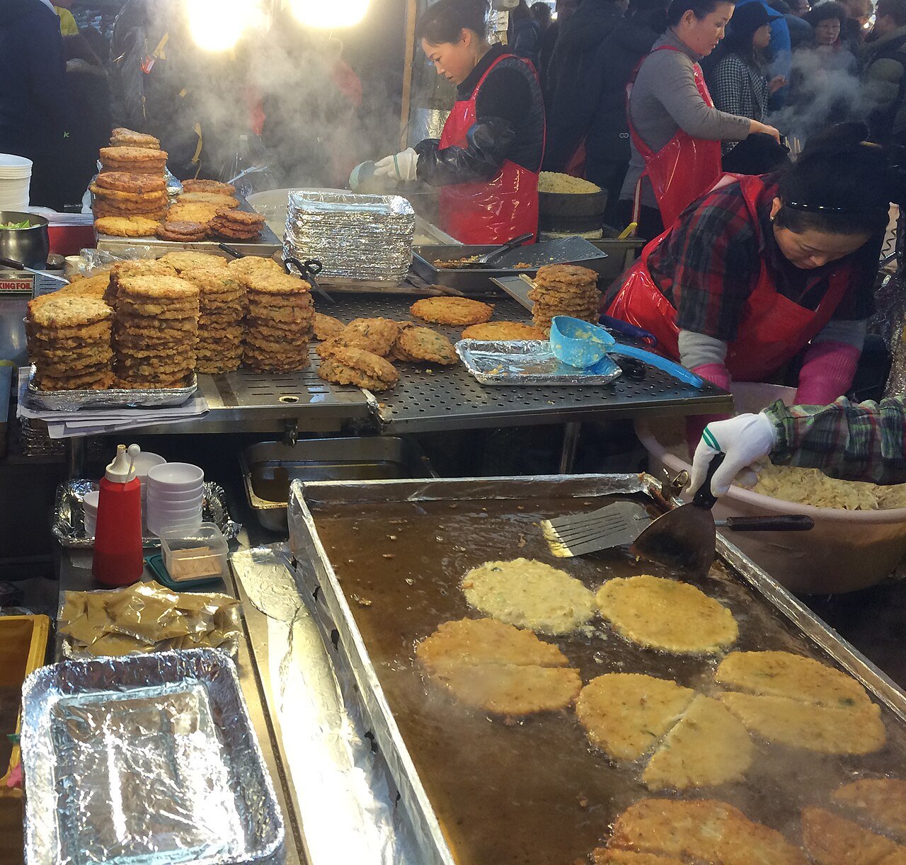 A vendor frying bindaetteok mung bean pancakes on a griddle at Gwangjang Market in Seoul