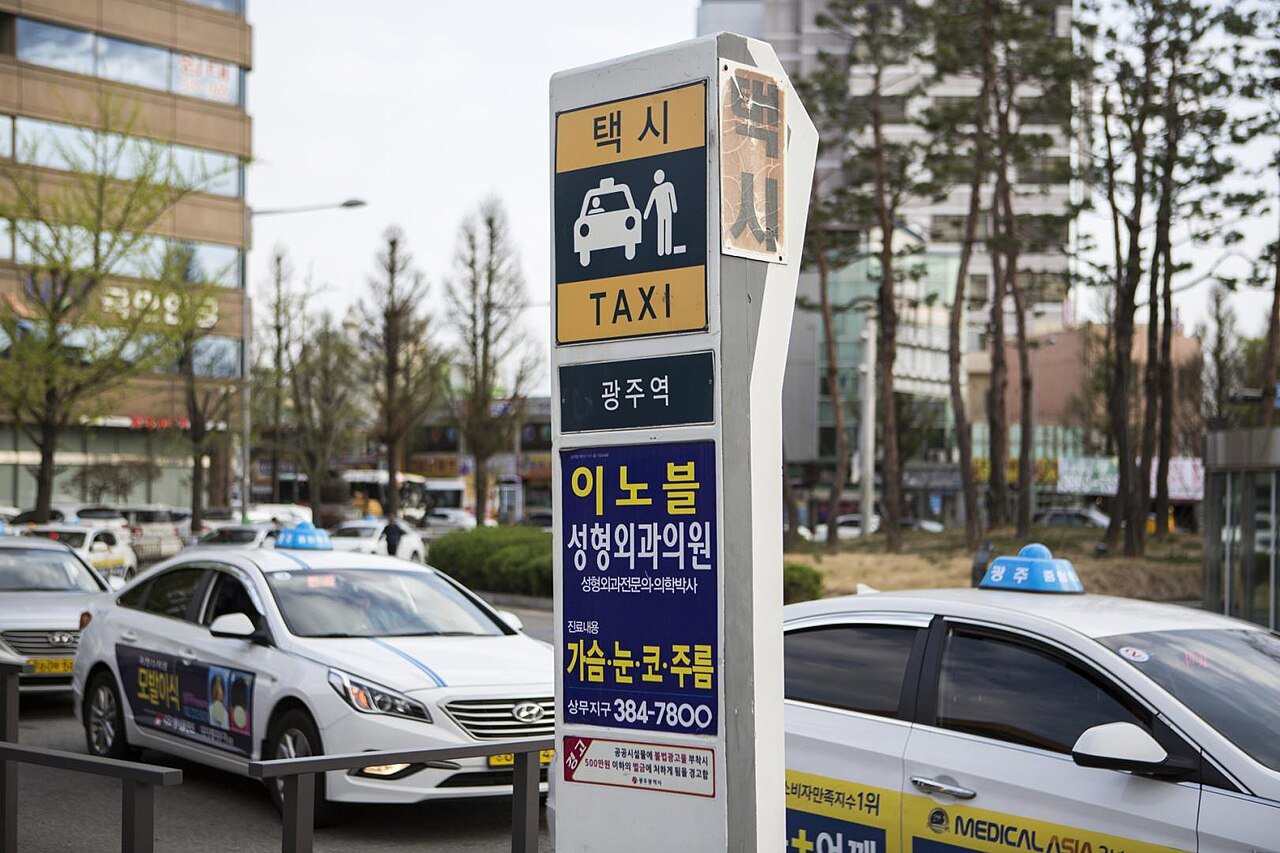 A taxi stand in Korea with a Taxi sign and taxis waiting