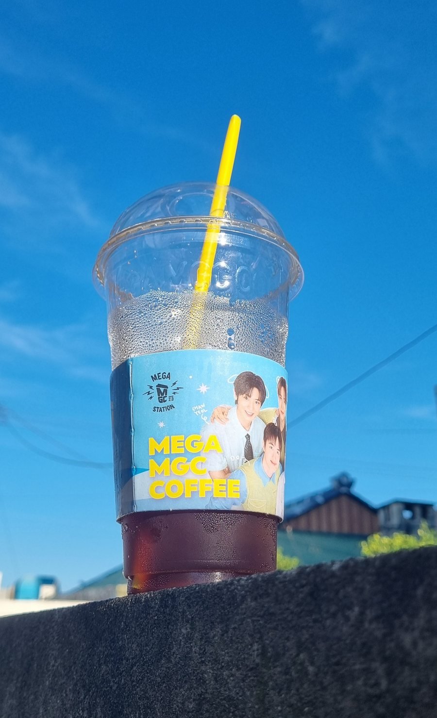A Mega MGC Coffee iced americano in a plastic cup against a blue sky