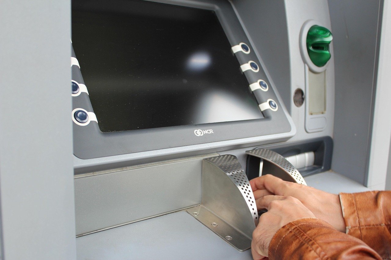 Hands using the keypad and cash slot of an ATM