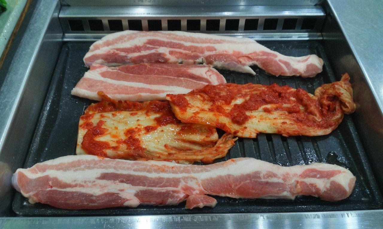 Raw pork belly strips and kimchi laid out on a Korean BBQ grill plate before cooking