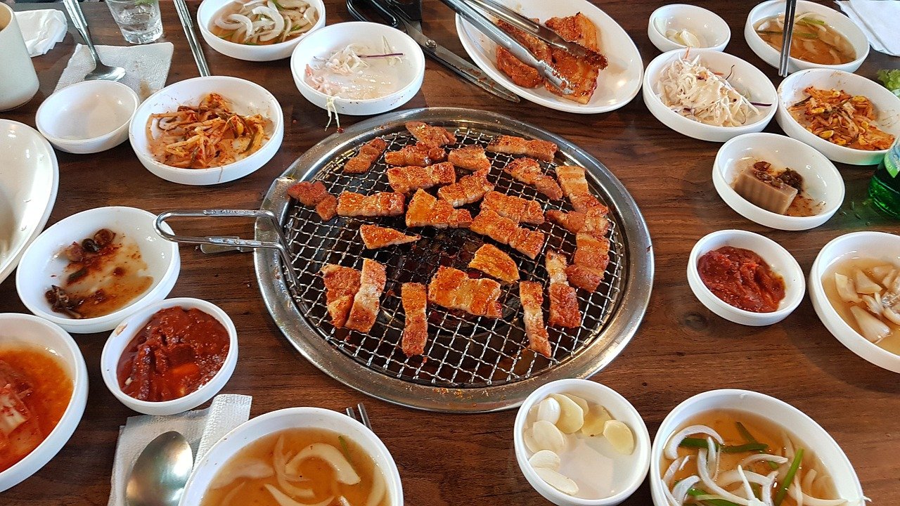 A full Korean BBQ table with pork belly on the centre grill ringed by more than a dozen free banchan side dishes