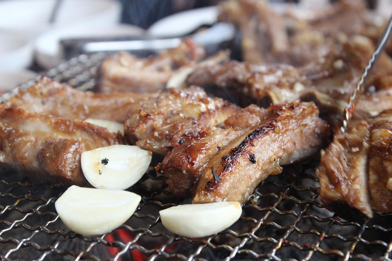 Marinated pork ribs and whole garlic cloves grilling over charcoal