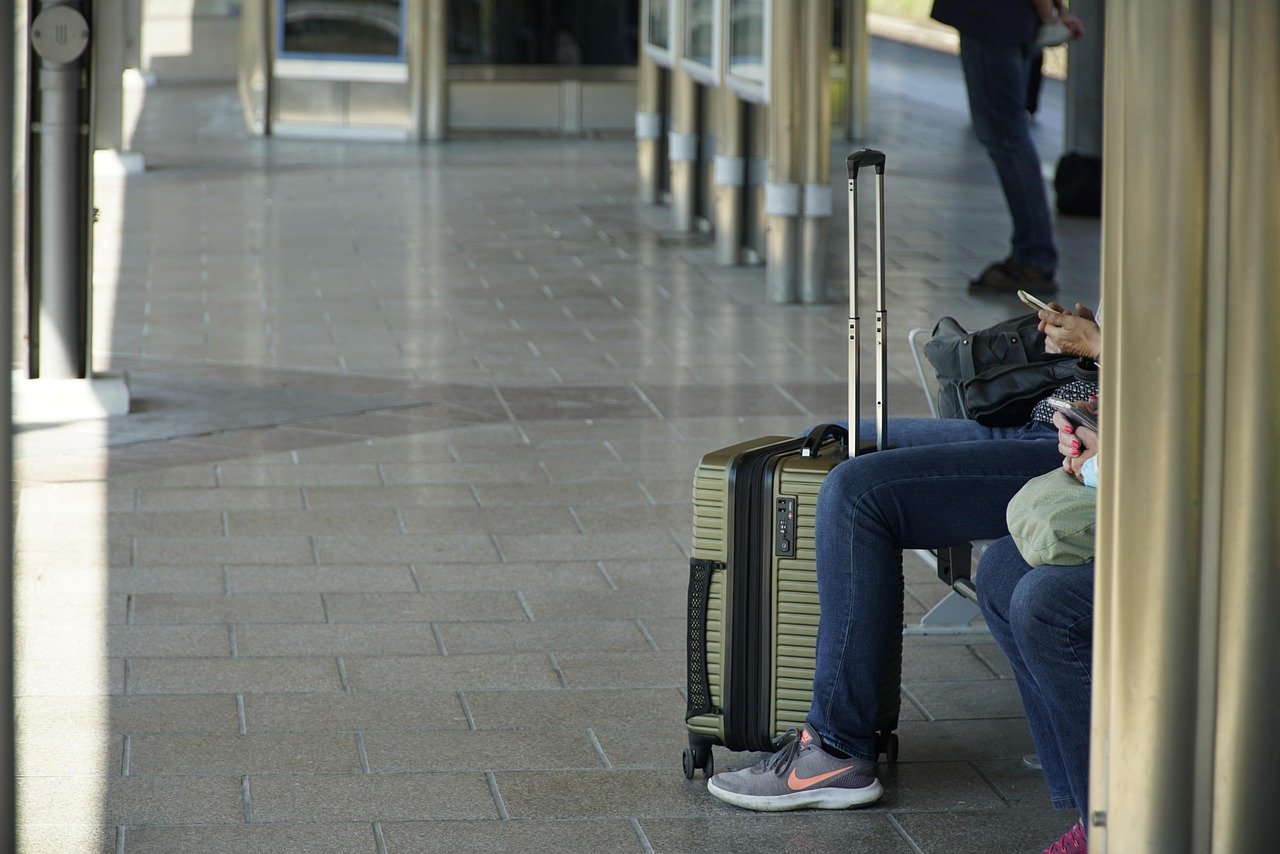Hard-shell carry-on suitcase next to a traveler waiting at a station