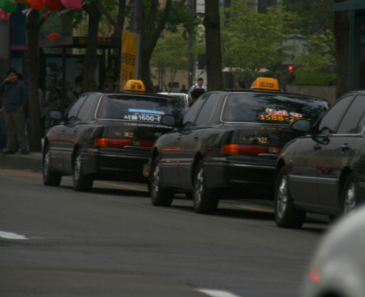 A line of black taxis with yellow roof signs waiting at the kerb in Seoul